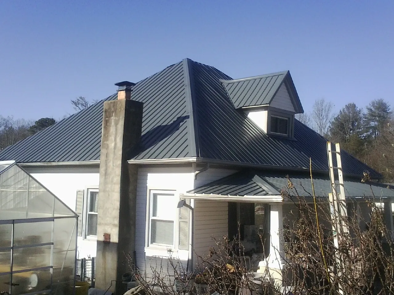 Dark blue standing seam metal roof on a white farmhouse with dormer — Slate & Tile Roof Repair by Roofing Brothers in Woodhaven