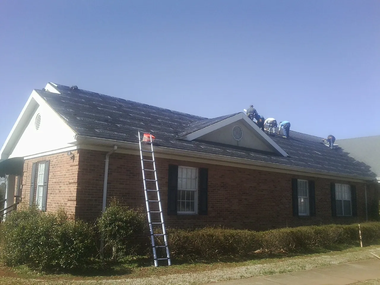 Crew tearing shingles off a brick ranch roof with a ladder set — Metal Roof Repair work by our crew in Woodhaven