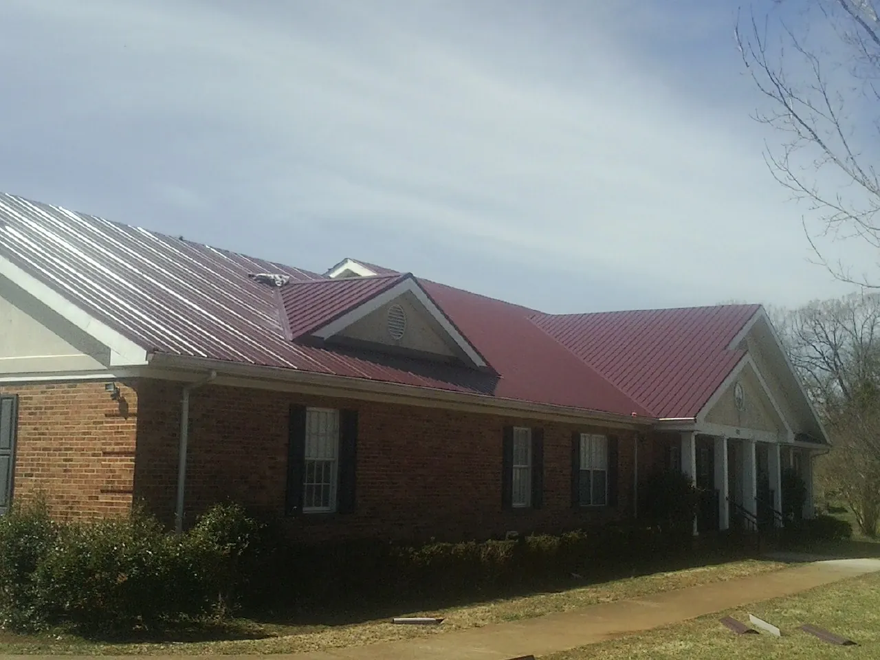 Red metal roof with gabled entries on a long brick building, from a Hail Damage Roof Repair job in Woodhaven