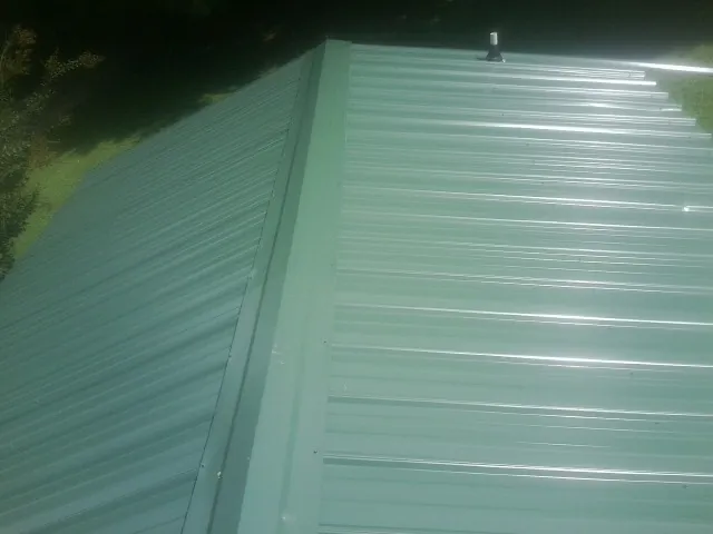 New green metal panels meeting at the ridge of a roof — Flat Roof Repair work by our crew in Woodhaven