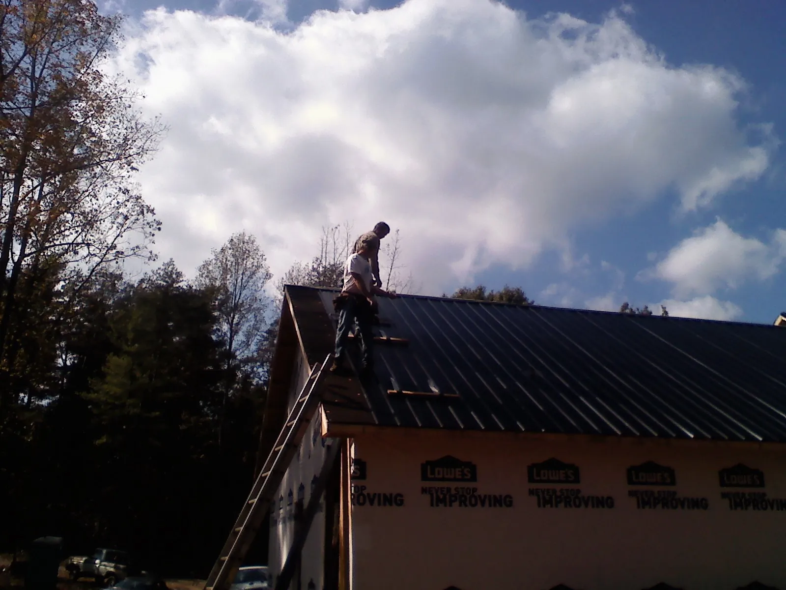 Roofer fastening dark metal panels high against a cloudy sky, from a Roof Inspection job in Woodhaven