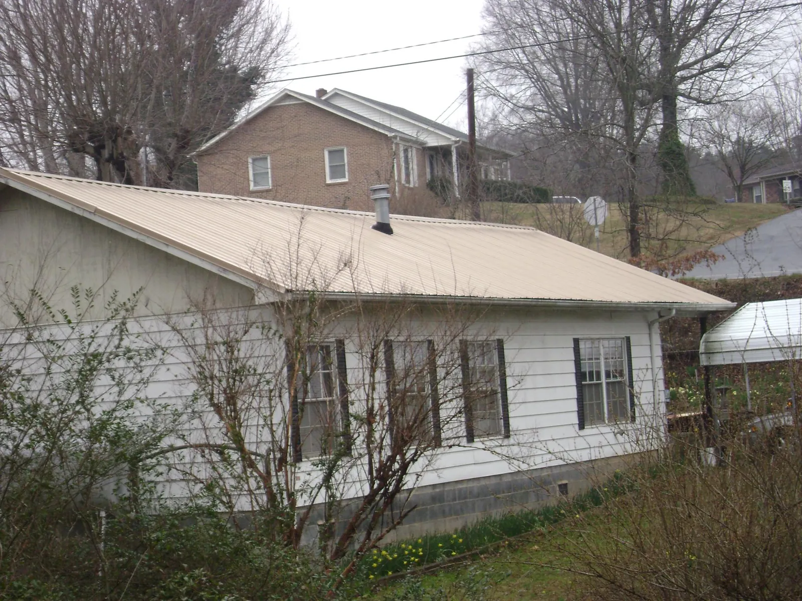 Tan metal roof on a white sided house set into a hillside — Commercial Roofing by Roofing Brothers in Woodhaven